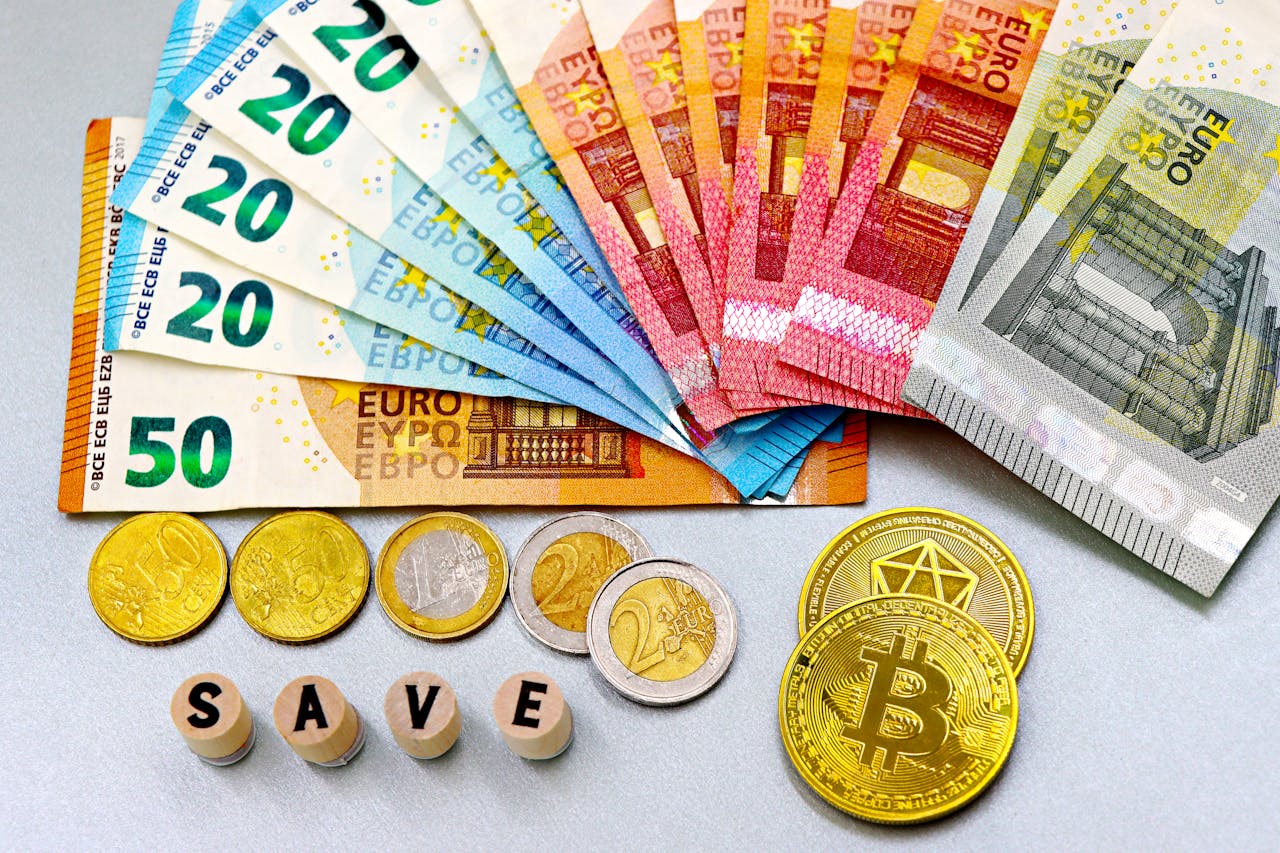 Euro banknotes and cryptocurrency coins arranged on a white surface with blocks spelling SAVE.